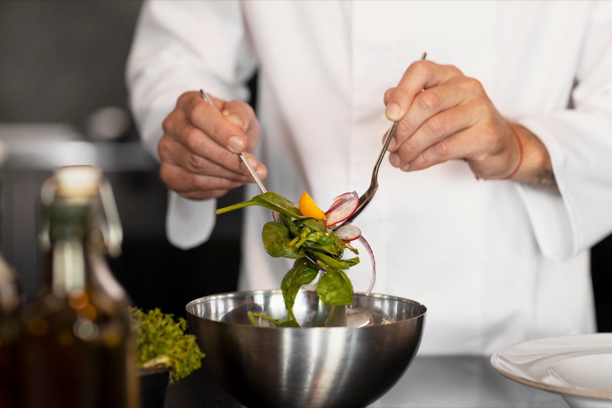 Küchenchef richtet einen frischen Salat in einer Edelstahlschüssel an